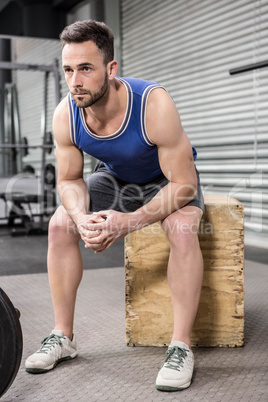 Muscular man sitting on wooden block