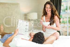 Young couple reading newspaper and having breakfast on bed