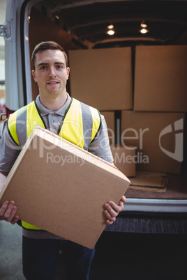 Delivery driver smiling at camera by his van holding parcel