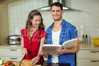 Woman cutting loaf of bread and man checking recipe book