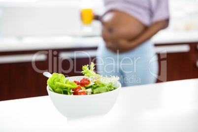 Pregnant woman in kitchen with salad on table