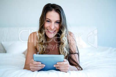 smiling woman lying on her bed on her tabet