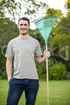 Portrait of young man standing with a gardening rake