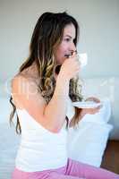 thoughtful woman drinking coffee on her bed