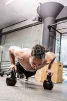 Shirtless man doing push up with kettlebells