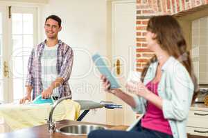 Woman using tablet and man ironing clothes