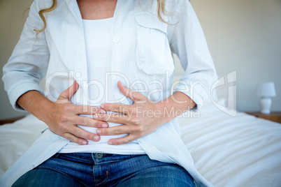 woman sitting on her bed clutching her stomach