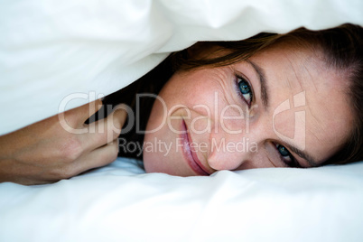 smiling woman peering  out from under a duvet