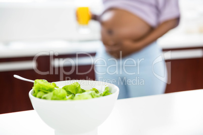 Pregnant woman in kitchen with salad on table
