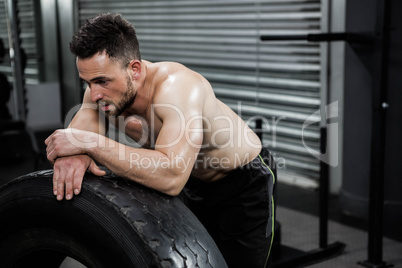 Tired shirtless man leaning against heavy tire