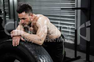 Tired shirtless man leaning against heavy tire
