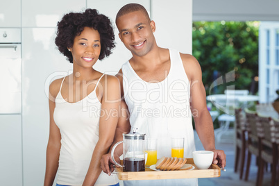 Happy couple holding breakfast tray in the kitchen