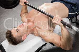 Shirtless man lifting heavy barbell on bench