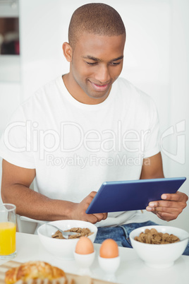 Young man using tablet and eating breakfast in kitchen