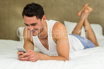 Young man lying on bed with his phone