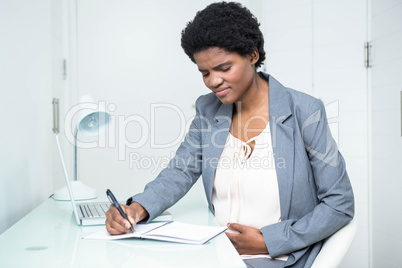 Pregnant businesswoman writing on notebook