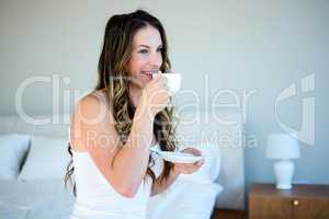 smiling woman sipping coffee on her bed