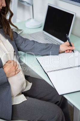 Pregnant businesswoman writing in folder