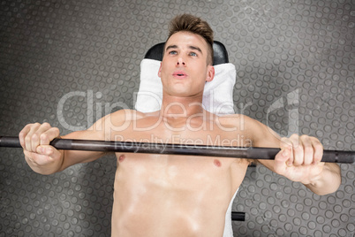 Shirtless man lifting heavy barbell on bench