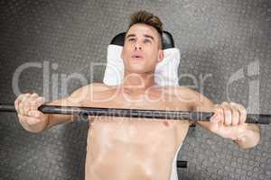 Shirtless man lifting heavy barbell on bench