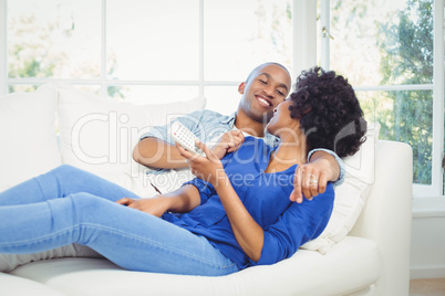 Happy couple lying on the sofa holding remote