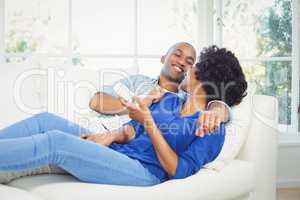 Happy couple lying on the sofa holding remote