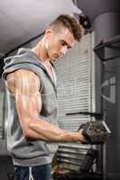Muscular man with grey jumper lifting dumbbell