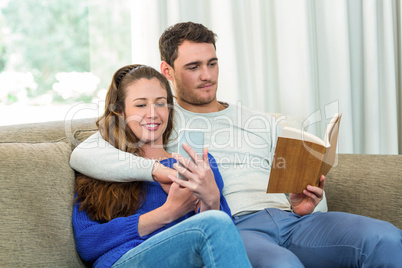 Young couple sitting on sofa and using mobile phone