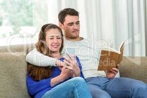 Young couple sitting on sofa and using mobile phone
