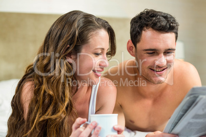 Young couple reading newspaper on bed