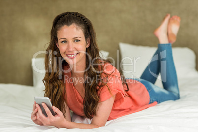 Young woman lying on bed with her phone