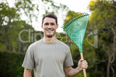 Portrait of young man standing with a gardening rake