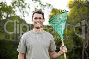 Portrait of young man standing with a gardening rake