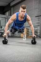 Muscular man doing push up with kettlebells