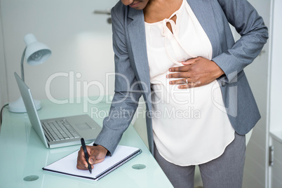 Pregnant businesswoman writing on notebook