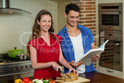 Portrait of woman cutting loaf of bread and man checking recipe
