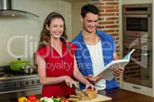Portrait of woman cutting loaf of bread and man checking recipe