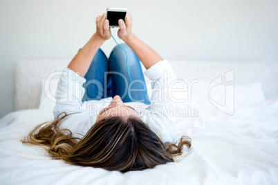 woman lying on her bed looking at her phone and listening to mus