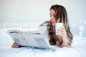 womaan lying in bed reading the newspaaper
