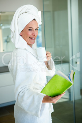 woman wearing a dressing gown reading a book and drinking a cup