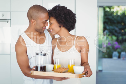 Happy couple holding breakfast tray in the kitchen