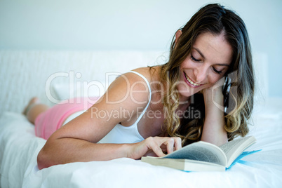 smiling woman reading a book in bed