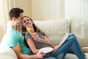 Young couple having croissant while reading newspaper