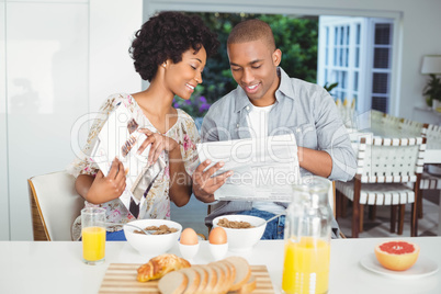 Smiling couple reading magazine and documents during breakfast