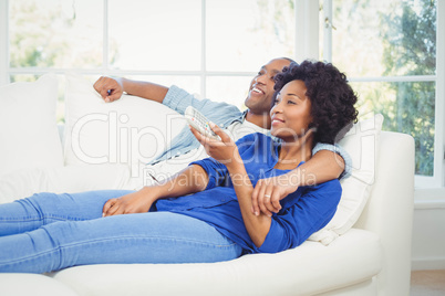 Happy couple lying on the sofa holding remote