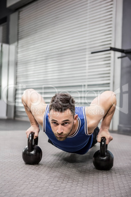 Muscular man doing push up with kettlebells