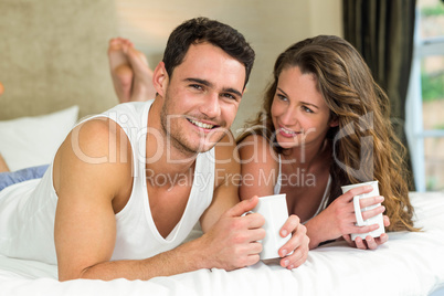 Young couple having cup of coffee on bed