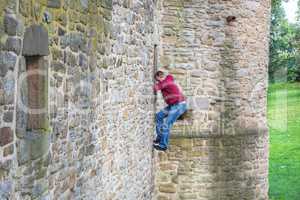 Mann klettert eine Burgmauer hinauf.