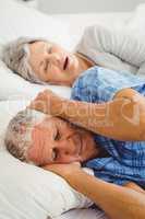 Senior man covering her ears while woman snoring