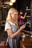 Smiling blonde drinking coffee and using smartphone